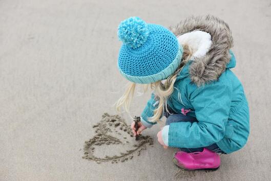 A little girl drawing in the sand.